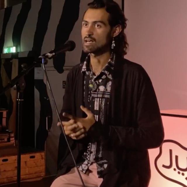 Photo of Pascal Michael speaking into a microphone on stage